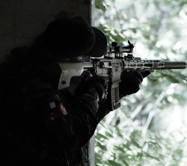 airsoft player aiming in the distance from a cover