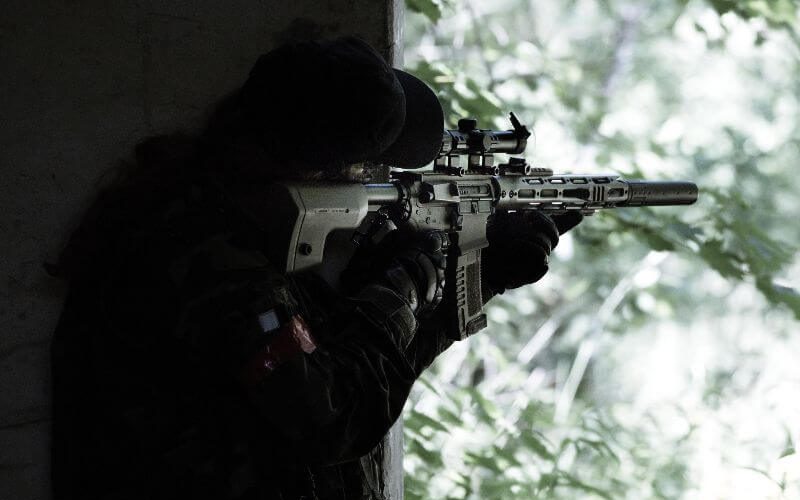 airsoft player aiming in the distance from a cover