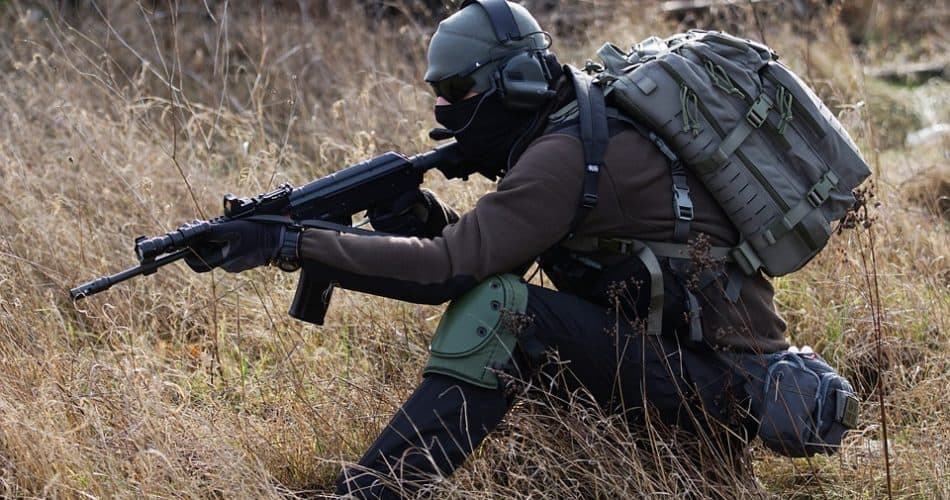 a man in airsoft gear kneeling in the grass