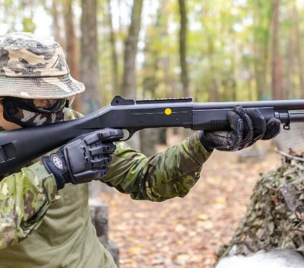 Player aiming a pump-action airsoft shotgun in woodland